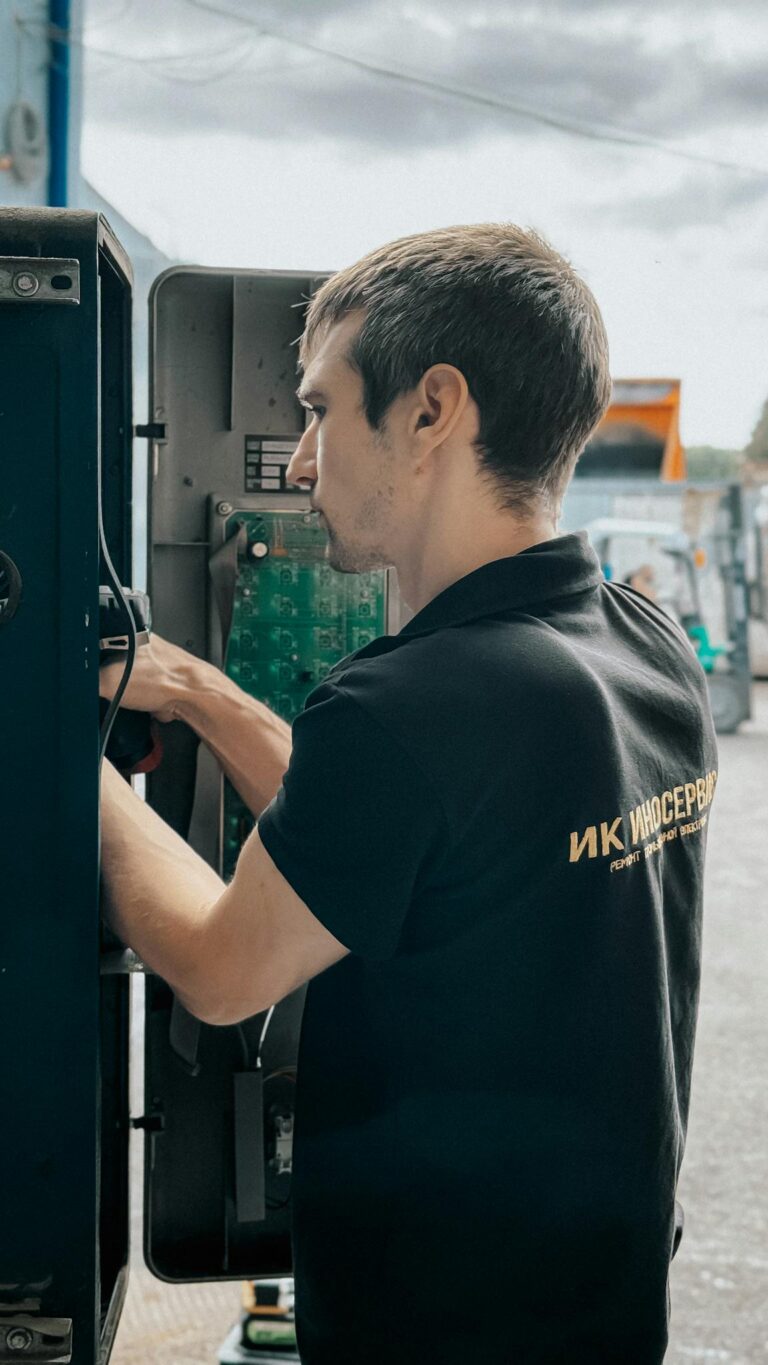 Technician repairing electrical panel outdoors on a cloudy day, focused on internal components.