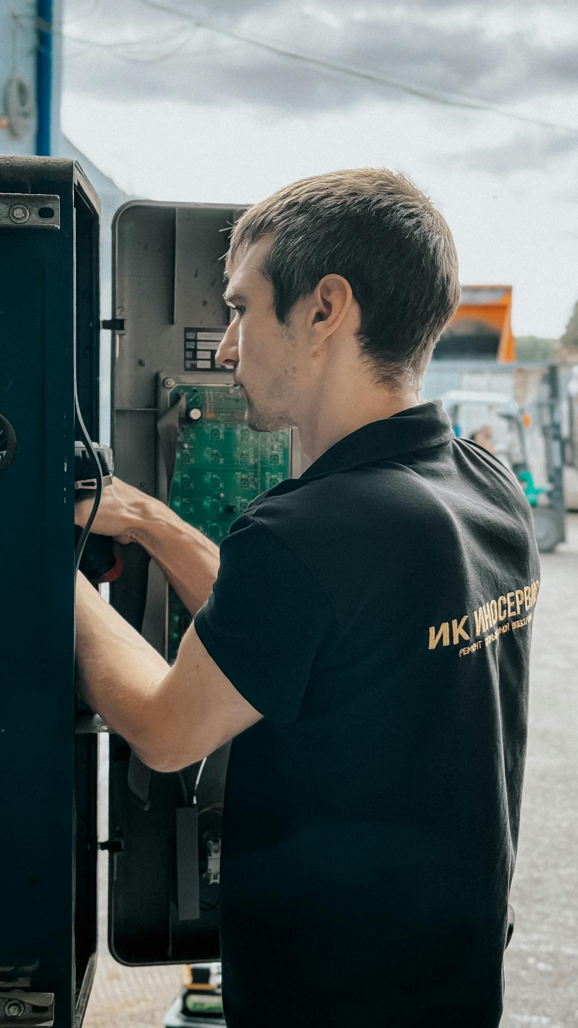 Technician repairing electrical panel outdoors on a cloudy day, focused on internal components.